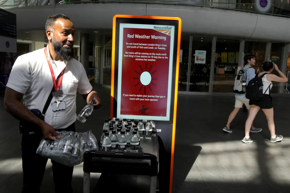 FILE - A railway worker hands out bottles of water to passengers at King's Cross railway station where there are train cancellations due to the heat in London, July 19, 2022, during a heat wave. The United Nations says weather disasters costing $200 million a day and irreversible climate catastrophe looming show the world is “heading in the wrong direction.” (AP Photo/Kirsty Wigglesworth, File)