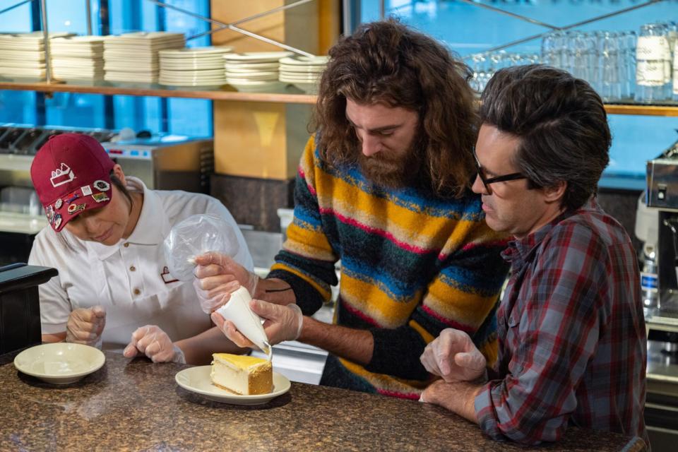 Hosts Charles "Link" Neal and Rhett McLaughlin work with Cheesecake Factory employee PJ Starr, as seen on Inside Eats with Rhett and Link, Season 1.