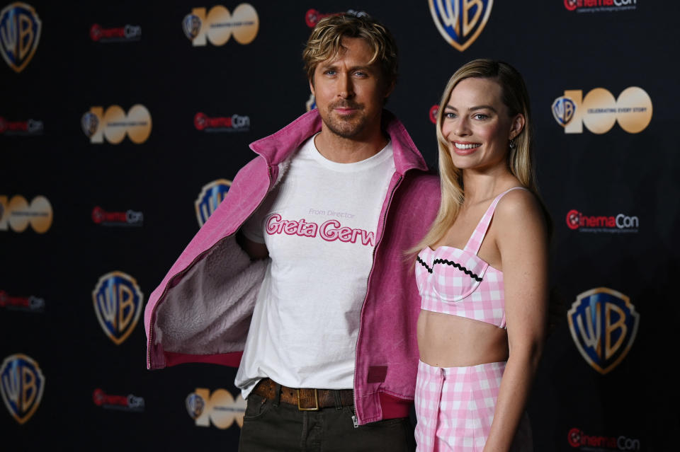 Ryan Gosling, in pink jacket, and Margot Robbie in a pink check bra with bare midriff pose on the red carpet.