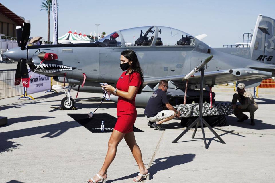 A woman walks past a Beechcraft AT-6 Wolverine light-attack aircraft as crew install a device to its wing at the Dubai Air Show in Dubai, United Arab Emirates, Sunday, Nov. 14, 2021. The biennial Dubai Air Show opened Sunday as commercial aviation tries to shake off the coronavirus pandemic. (AP Photo/Jon Gambrell)
