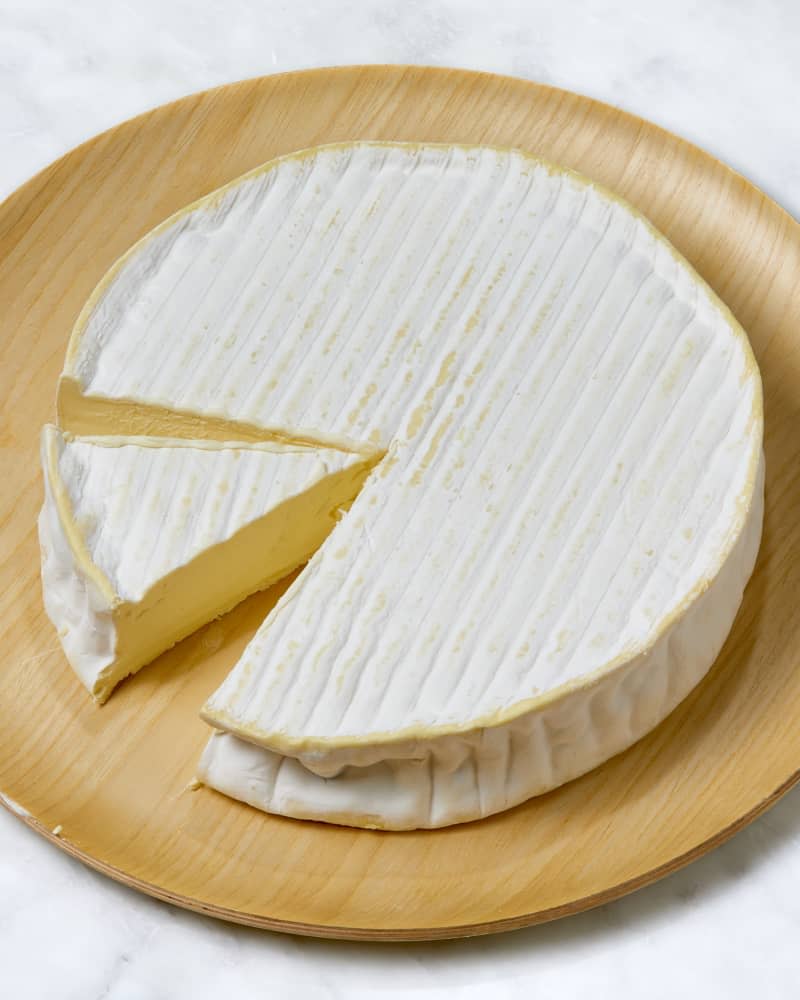 Angled shot of cut brie on a wooden plate.