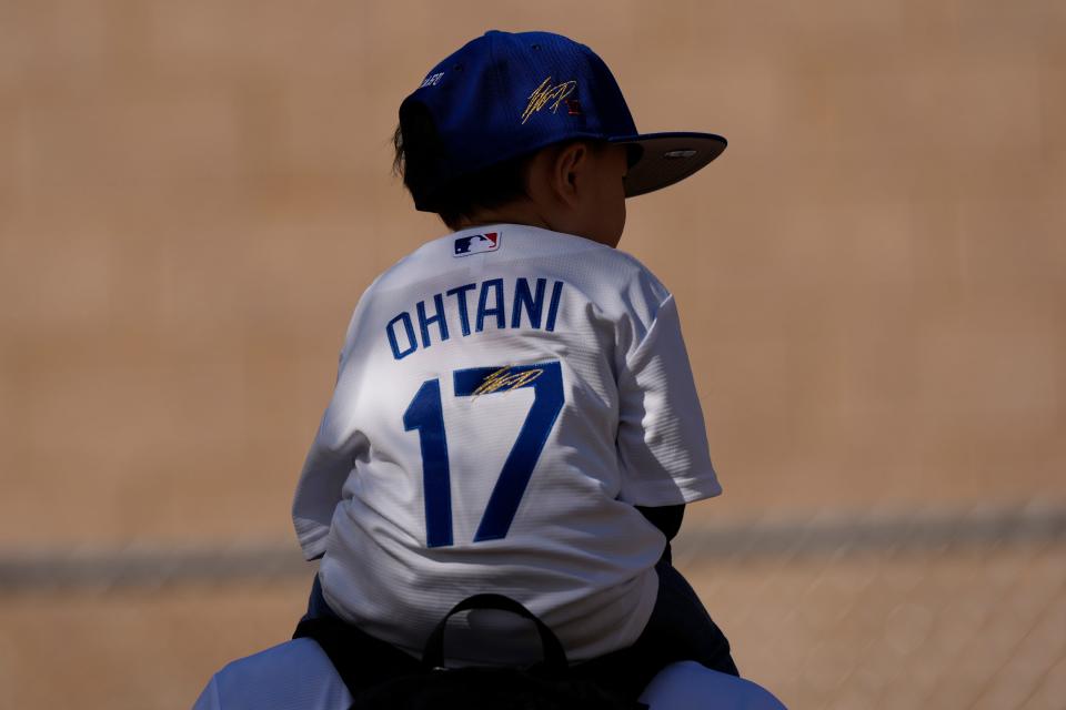 A child wearing a Shohei Ohtani jersey and cap sits on their father's shoulders on the first day of spring training.