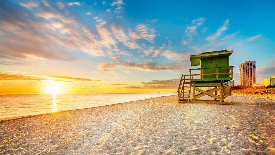 Miami South Beach sunrise with lifeguard tower and coastline with colorful cloud and blue sky.