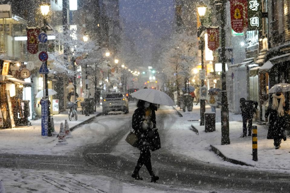 FILE - People walk along a shopping street as the snow comes down, Jan. 6, 2022, in Tokyo. The risk of typhoons in Japan has gone up and the amount of snowfall has declined, even as the threat of heavy snowfall remains. (AP Photo/Kiichiro Sato, File)