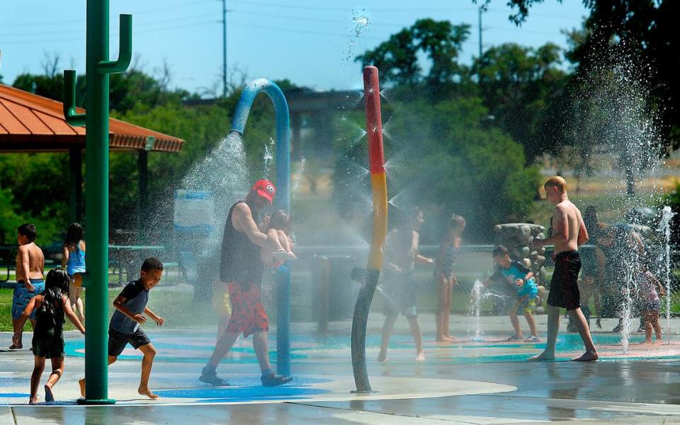 Children and adults cool off under the sprayers at the splash pad at the Playground of Dreams in Kennewick’s Columbia Park.