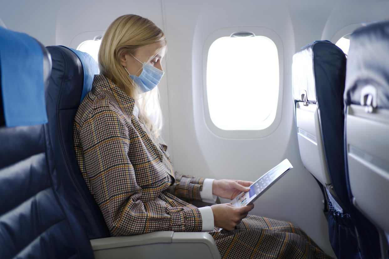 Portrait of young beautiful woman with long blond hair wearing mask inside airplane while reading safety instructions.