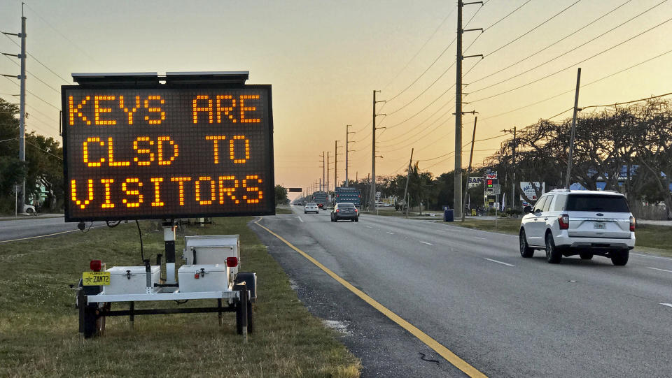 In this photo provided by the Florida Keys News Bureau, cars pass an electronic messaging board on the Florida Keys Overseas Highway, Wednesday, March 25, 2020, in Key Largo, Fla. The coronavirus crisis has spurred Florida Keys officials to shut down the subtropical island chain to visitors until further notice. To reinforce the message, the Monroe County Sheriff's Office is planning to implement southbound traffic stops in the next day or two at the top of the Keys. (Andy Newman/Florida Keys News Bureau via AP)