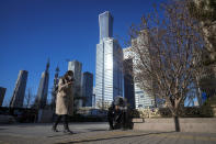 A woman walks by a man taking a rest along a quiet walkway against the office buildings at the central business district in Beijing, Monday, Dec. 5, 2022. China is easing some of the world's most stringent anti-virus controls and authorities say new variants are weaker. But they have yet to say when they might end a "zero-COVID" strategy that confines millions of people to their homes and set off protests and demands for President Xi Jinping to resign. (AP Photo/Andy Wong)