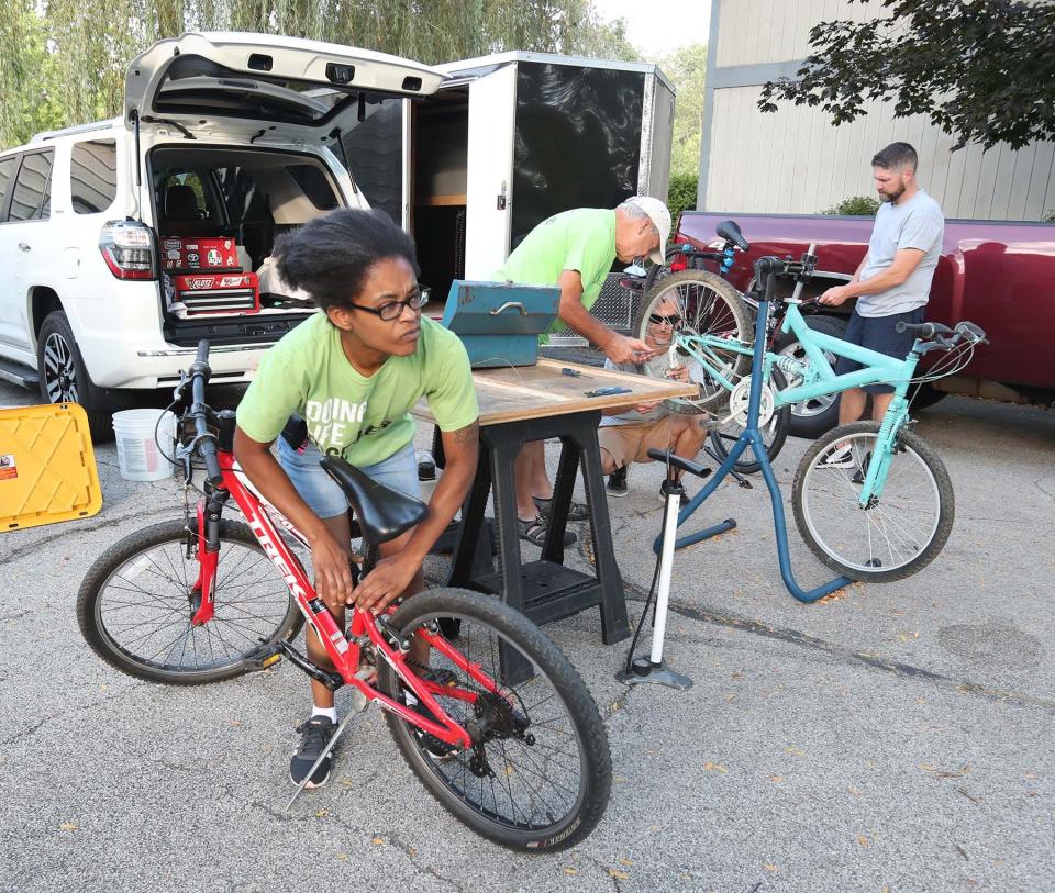 Terah Coleman works on her bike at the bicycle workshop that members of her church, The Chapel's Green Campus, have set up at her apartment complex as part of their Bike Ministry. Matthew Long, Kent Bender and Dusty Dannemiller are working on residents' bikes as Coleman is able to use the group's tools to adjusts her bike seat.