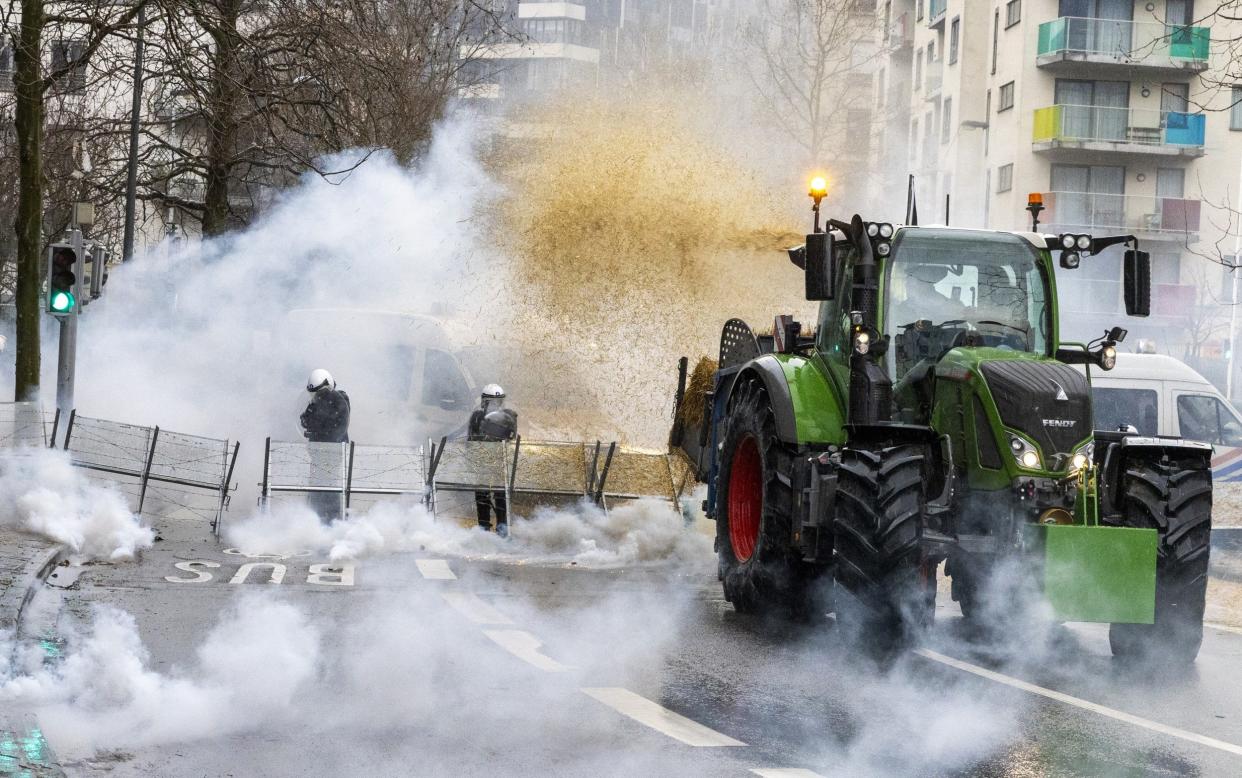 A farmer emits hay from his tractor onto Belgian riot police officers as gas rises from tear gas canisters