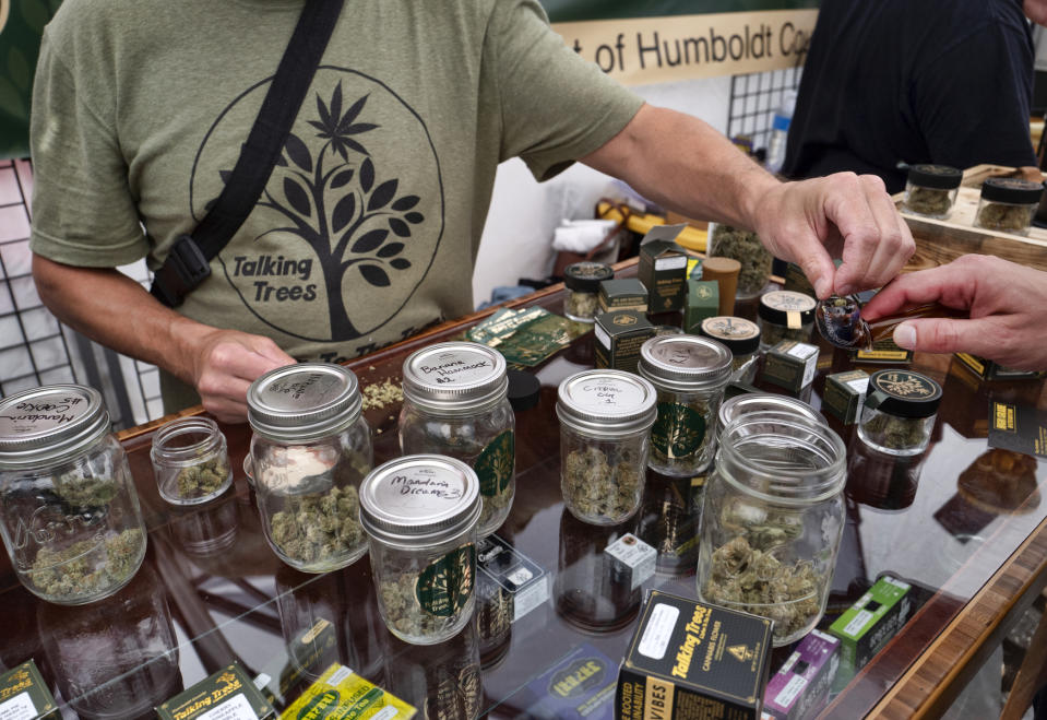 In this Thursday, June 20, 2019 photo a vendor with Talking Trees Farms a Northern Humboldt County sustainable cannabis farm, offers a taste of their latest crop of crafted marijuana flower to an attendee in the farmers market during a business to business networking event, WeedCon West 2019 in Los Angeles. Marijuana shoppers are going to be getting a message from California regulators: Go legal. (AP Photo/Richard Vogel)