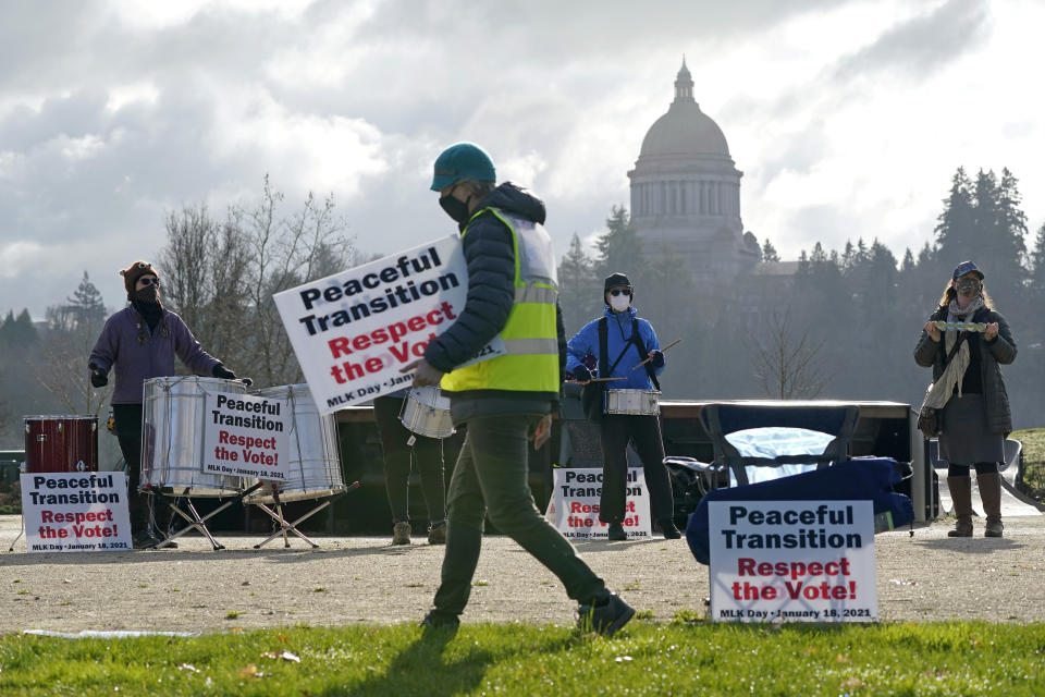 A person walks with a sign near a drum circle during a vigil supporting a peaceful transition from President Donald Trump to President-elect Joe Biden, Monday, Jan. 18, 2021, in Olympia, Wash. More than 100 people took part in the demonstration ahead of Biden's upcoming inauguration on Wednesday. (AP Photo/Ted S. Warren)