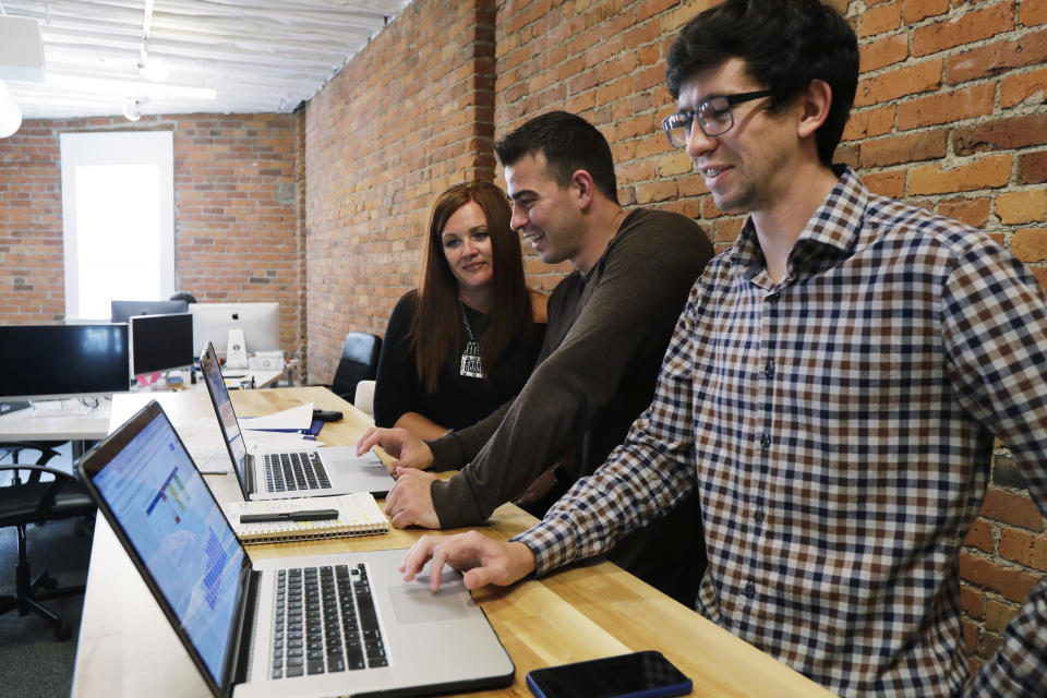 In this Tuesday, Sept. 10, 2019, photo Shane Griffiths, right, and Trenton Erker, center, co-owners of the digital marketing company Clarity Online, work with one of their clients, Susan Leeming, the owner of High Maintenance Spa and Salon in Tacoma, Wash., in their company's workspace in Seattle. Griffiths and Erker use technology for tasks like billing, scheduling appointments, tracking the time they spend on clients' projects and putting together reports on visits to client websites, as well as using freelancers for other tasks as ways to save money on employment costs, and also have more flexibility when they need specific talents or expertise for a project. (AP Photo/Ted S. Warren)