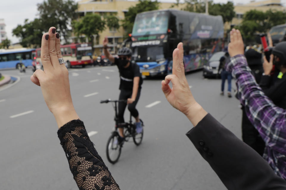 A man on a bicycle greets protesters with a three-fingered salute, a symbol of resistance, as people gather for a protest near Democracy Monument in Bangkok, Thailand, Wednesday, Oct. 14, 2020. Thai activists hope to keep up the momentum in their campaign for democratic change with a third major rally in Bangkok on Wednesday. (AP Photo/Gemunu Amarasinghe)