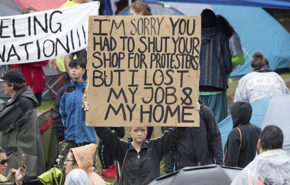 Protesters hold signs as they stand in wet conditions as they voice their opposition to coronavirus vaccine mandates at Parliament in Wellington, New Zealand, Saturday, Feb. 12, 2022. The protest began when a convoy of trucks and cars drove to Parliament from around the nation, inspired by protests in Canada. (Mark Mitchell/NZME via AP)