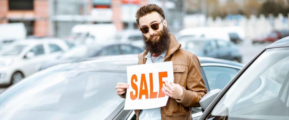 Stylish bearded salesman with sales plate near the cars on the open ground of a dealership