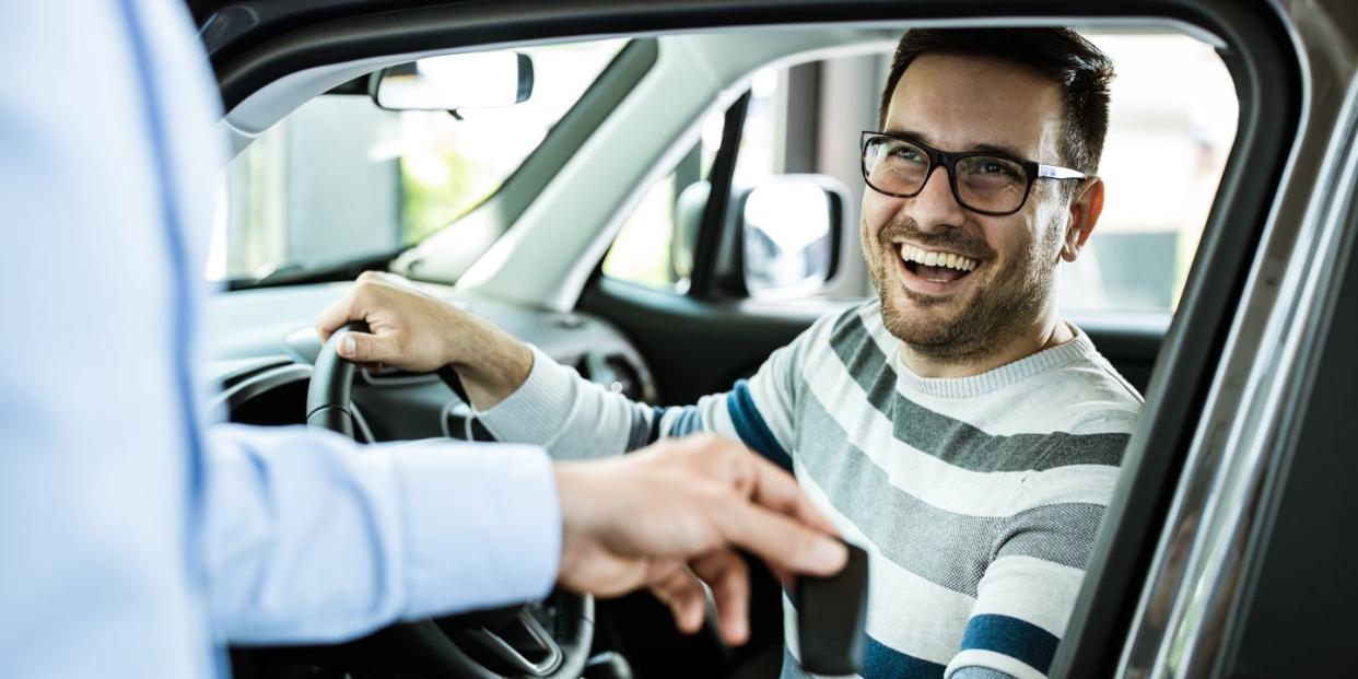 young happy man receiving new car keys in a showroom