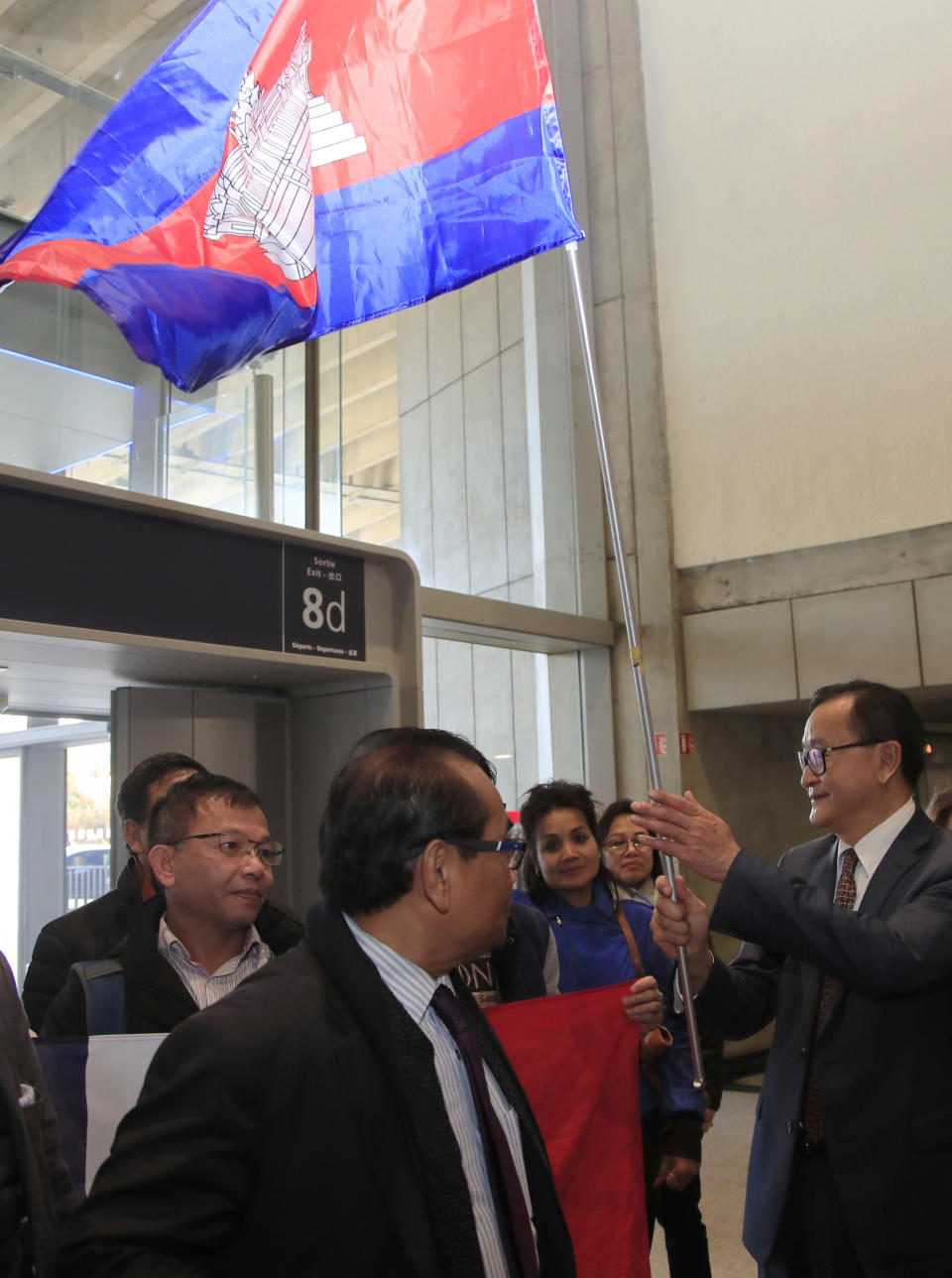 Cambodia's most prominent opposition politician Sam Rainsy greets supporters with the national flag as he attempted to return to Cambodia Thursday, Nov. 7, 2019 at Charles de Gaulle airport, north of Paris. Cambodia's main opposition figure Sam Rainsy said he was turned away from boarding a Thai Airways flight from Paris-Bangkok in his attempt to return to Cambodia from his self-imposed exile to challenge the longtime leader there. (AP Photo/Michel Euler)