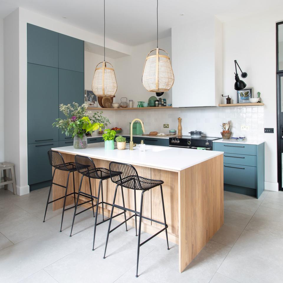 A wooden kitchen island with a white countertop, black stools and hanging pendant lights.