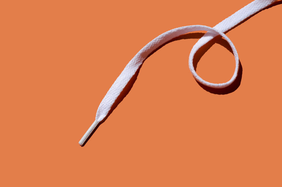 A white shoelace against an orange background, partially curled into a loop