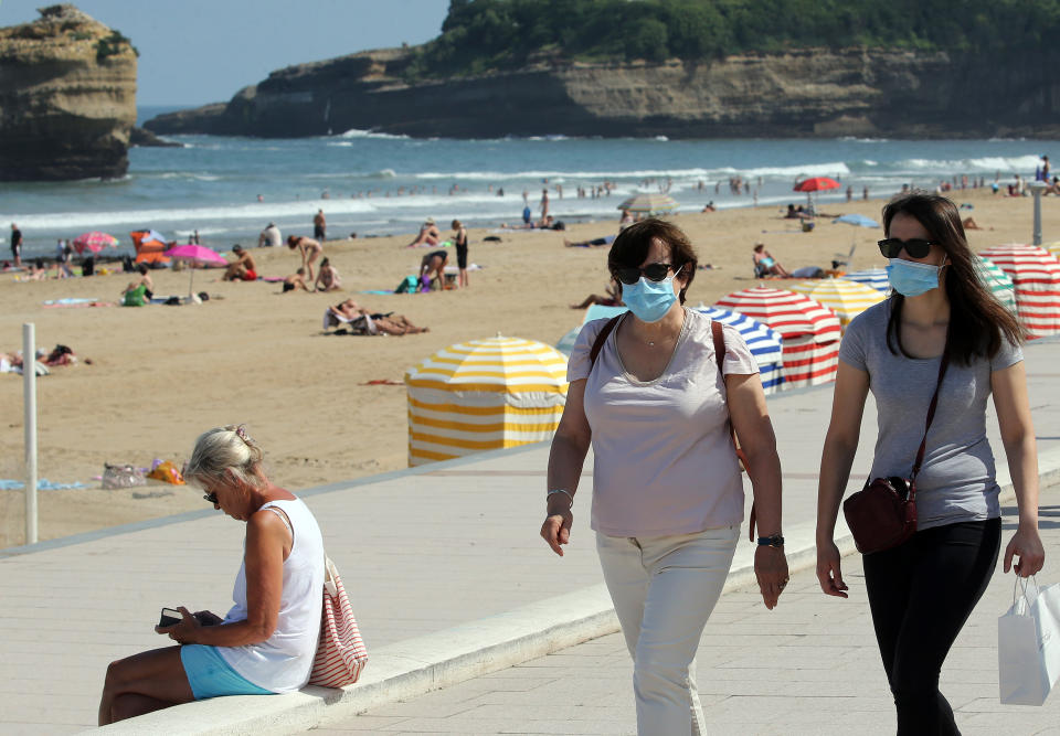 People wear face masks as they walk near the beach in Biarritz, southwestern France, Tuesday, July 21, 2020. Face masks are now obligatory in France's supermarkets, shopping malls, banks, stores, and indoor markets, to curb worrisome signs that the coronavirus is making inroads again. (AP Photo/Bob Edme)