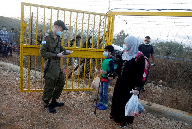 An Israeli soldier checks the documents of Palestinians crossing through the gate of a fence, part of the Israeli barrier, as they make their way towards an olive field, in Salfit in the Israeli-occupied West Bank