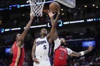 Sacramento Kings guard De'Aaron Fox (5) drives to the basket between New Orleans Pelicans forwards Brandon Ingram (14) and Herbert Jones in the first half of an NBA basketball play-in tournament game in New Orleans, Friday, April 19, 2024. (AP Photo/Gerald Herbert)