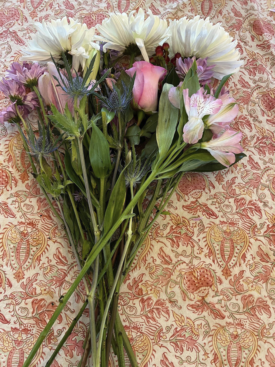This May 1, 2024 image provided by Jessica Damiano shows a supermarket bouquet of three white chrysanthemums, a lily stem and a single rose embellished with greenery and "filler" flowers on Long Island, New York. Placing flowers in a decorative pitcher or vase is one way to elevate a floral arrangement. (Jessica Damiano via AP)