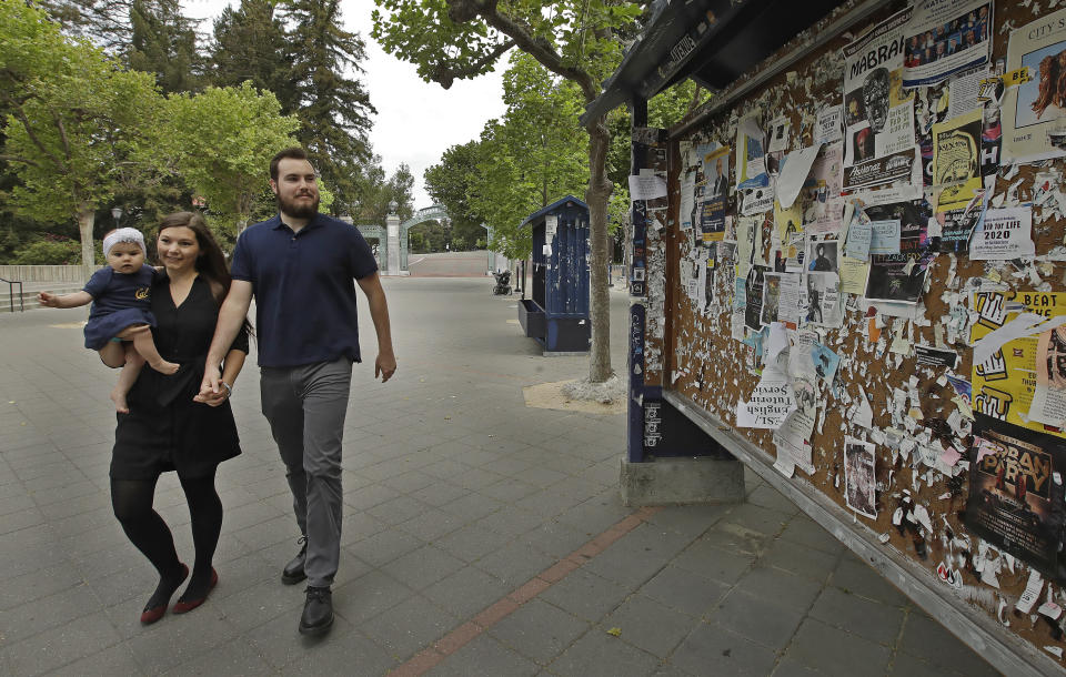 University of California at Berkeley graduate Tyler Lyson walks with his wife, Lucie, who is holding their 8-month-old daughter, Lisa, as they walk past a student activity billboard on the closed Cal campus in Berkeley, Calif., on Monday, May 11, 2020. The 28-year-old won a full scholarship to the University of California-Berkeley and will become the first in his family to earn a degree. “I’m supposed to be doing great,” he said. Instead, he feels powerless and panicked, with a political science degree that seems worthless. (AP Photo/Ben Margot)