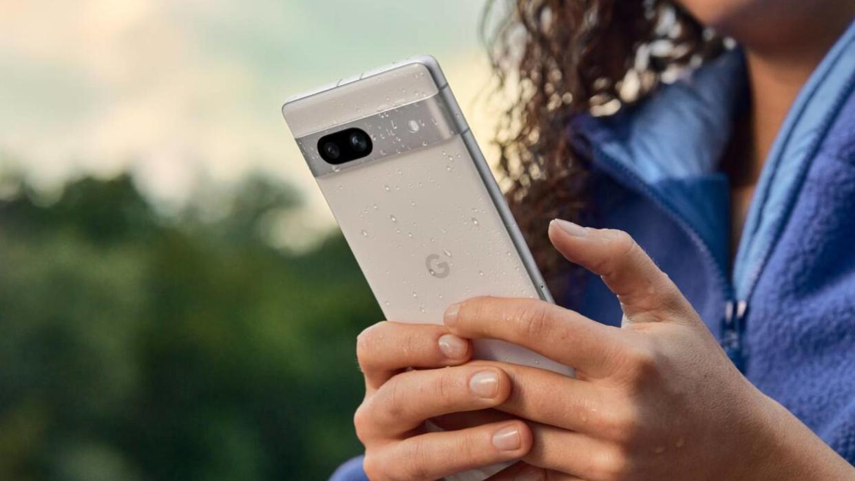  Woman holding Pixel 7a in snow with water droplets on it . 