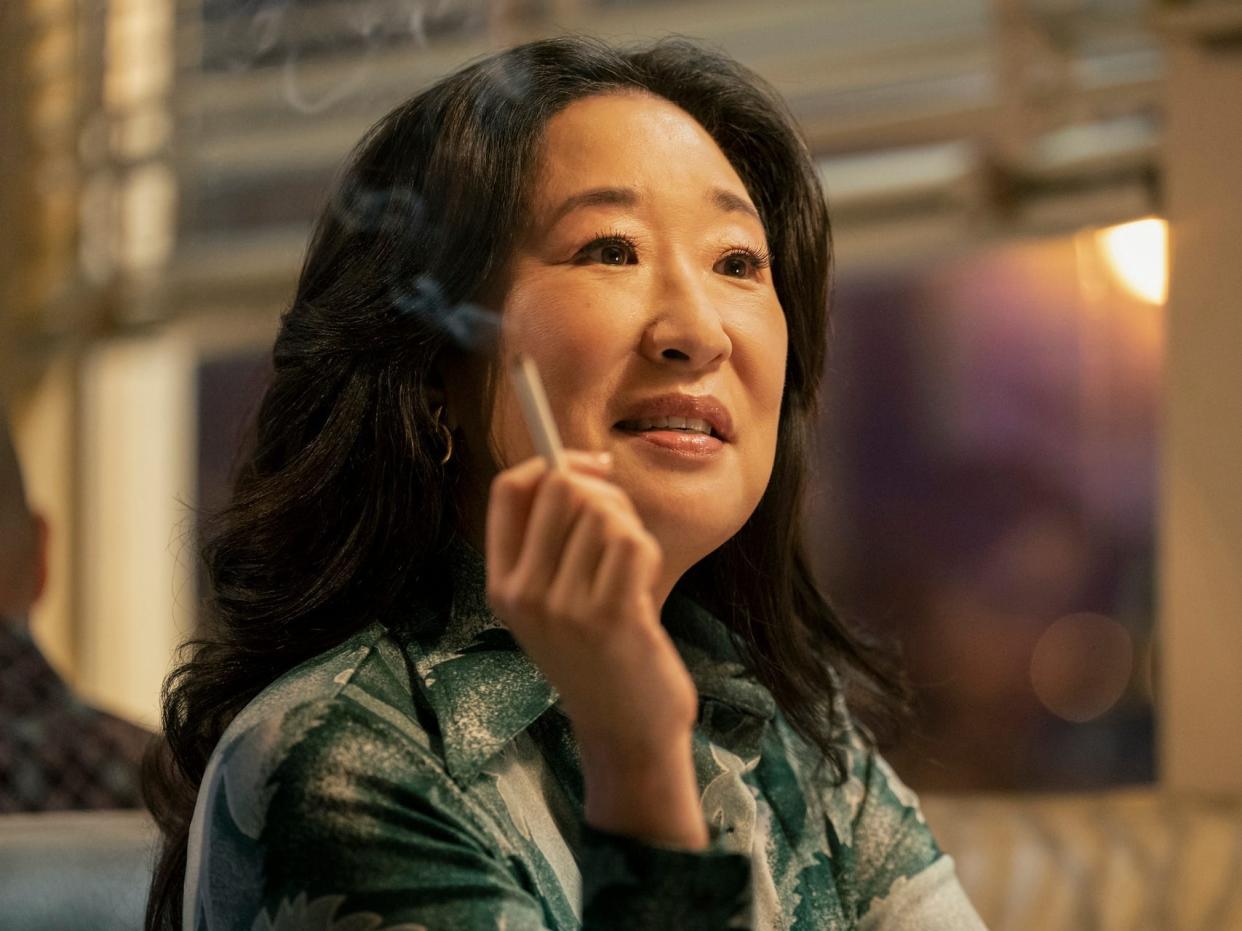 sandra oh in the sympathizer, her hair worn swept back and wavy ina 70s style, in a green shirt, and holding a cigarette