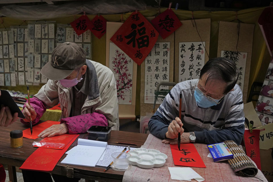 Calligraphy artists Josiah Lo, right, 81, and Chung, 90, write "Fai Chun," traditional decorations with Chinese calligraphy, which sell for HK$30 each (US $3.9), in Hong Kong on Jan. 26, 2022. In the runup to the Lunar New Year, calligraphers set up on the streets of Hong Kong to write ink-brush phrases on traditional red paper banners for homes and offices. (AP Photo/Kin Cheung)