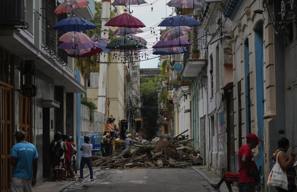 People watch firefighters clear debris from a building on Lamparilla street that partially collapsed inwardly, killing three people, as they search for survivors in Havana, Cuba, Wednesday, Oct. 4, 2023. The Cuban government has in the past acknowledged the problem of housing deterioration, but says the lack of material resources prevents it from tackling it. (AP Photo/Ramon Espinosa)