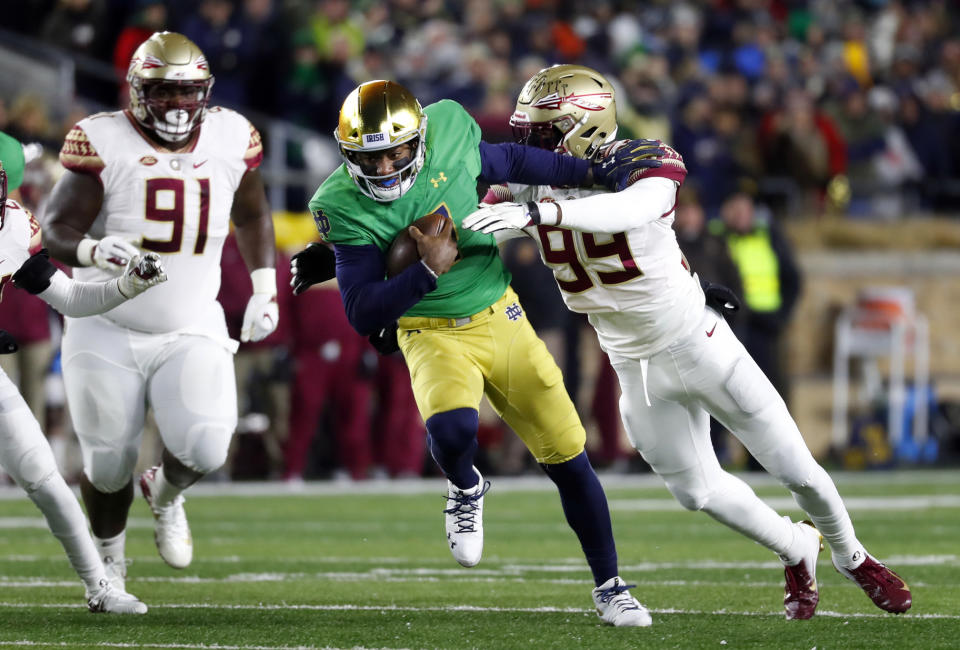 Notre Dame quarterback Brandon Wimbush, center, tries to break the tackle of Florida State defensive end Brian Burns, right, as Florida State defensive lineman Robert Cooper (91) watches in the first half of an NCAA college football game in South Bend, Ind.,Saturday, Nov. 10, 2018. (AP Photo/Paul Sancya)