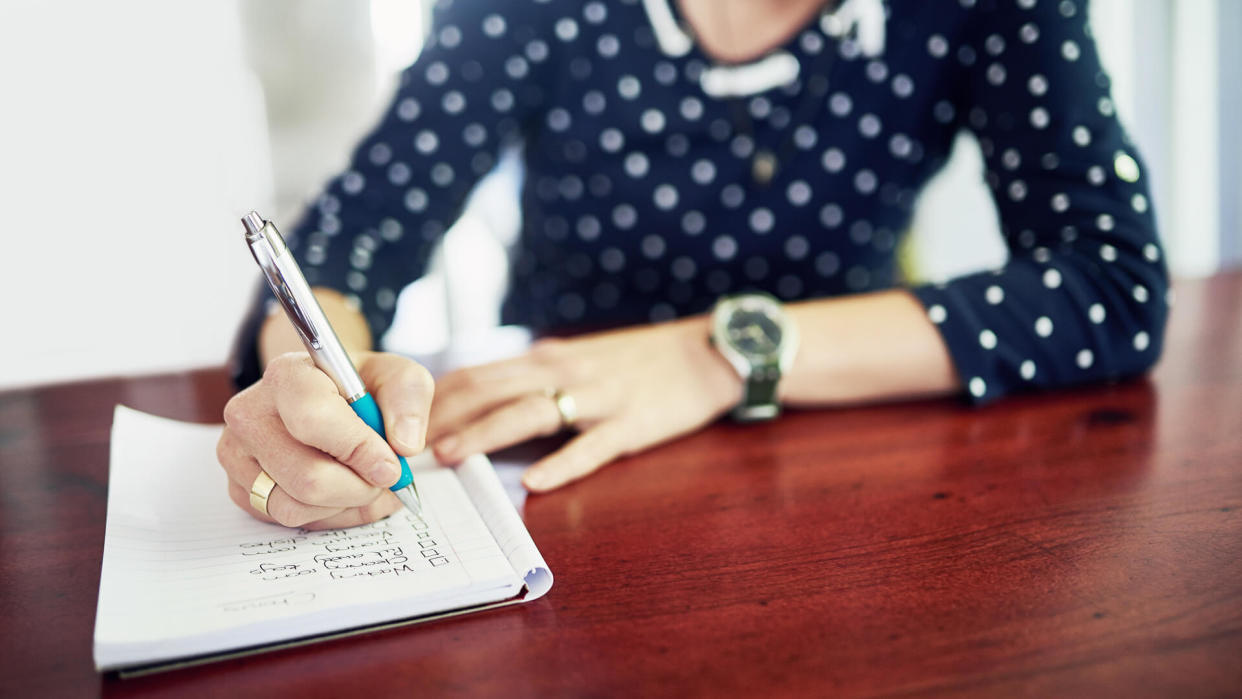 Shot of a woman writing in a book at a table.