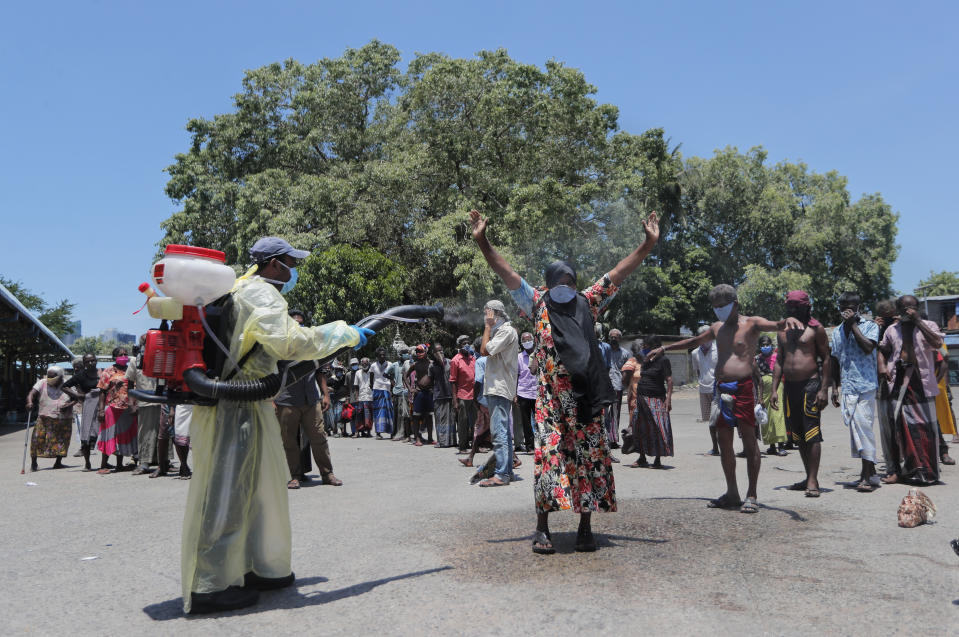 A Sri Lankan police officer disinfects a homeless woman, as others stand in a queue before they are transported to an isolation center as a measure to prevent the spread of the new coronavirus during a lockdown in Colombo, Sri Lanka, Friday, April 17, 2020. Sri Lankan authorities claim they have largely managed to prevent community spreading through proper identification and isolation of people who came into contact with COVID-19 patients. (AP Photo/Eranga Jayawardena)