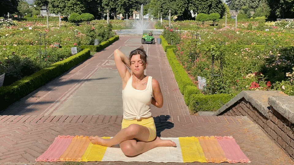 Woman seated on a yoga rug practicing stretches for the hips and shoulders