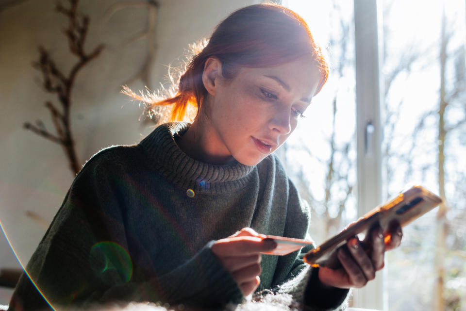 A person looking at their phone with a credit card in hand