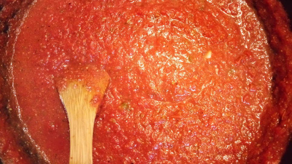 A wooden spoon stirring a pot of tomato sauce