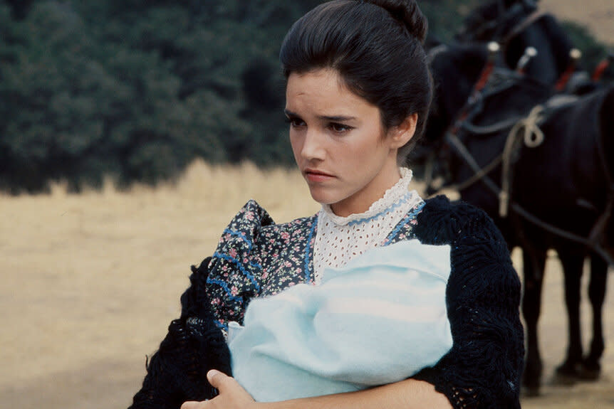 Brooke Adams holds a wrapped up baby while standing in front of a horse