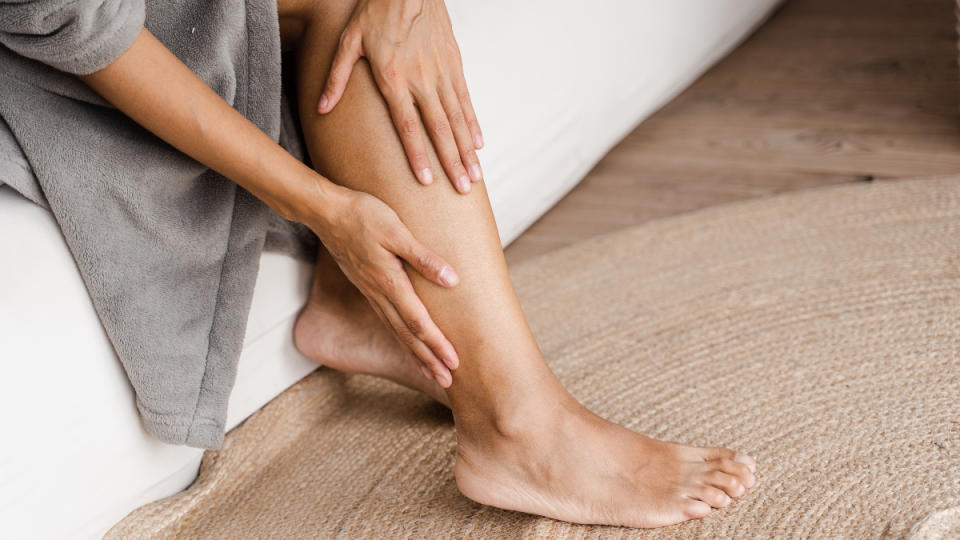 A close-up of  woman n a grey robe touching her hands to legs and feet