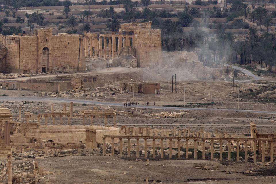 FILE -- In this April 14, 2016 file photo, Russian soldiers stand on a road as smoke rises from a controlled land mine detonation by Russian experts inside the ancient town of Palmyra, Syria in the central Homs province. Palmyra, the archaeological gem that Islamic State fighters retook Sunday, Dec. 11, 2016, from Syrian troops, is a desert oasis surrounded by palm trees, and a UNESCO world heritage site, that boasts 2,000-year-old towering Roman-era colonnades and priceless artifacts. It is also a strategic crossroads linking the Syrian capital, Damascus, with the country's east and neighboring Iraq. (AP Photo/Hassan Ammar, File)