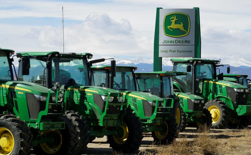 line of green john deere tractors in a dirt lot with snow capped mountains in the background
