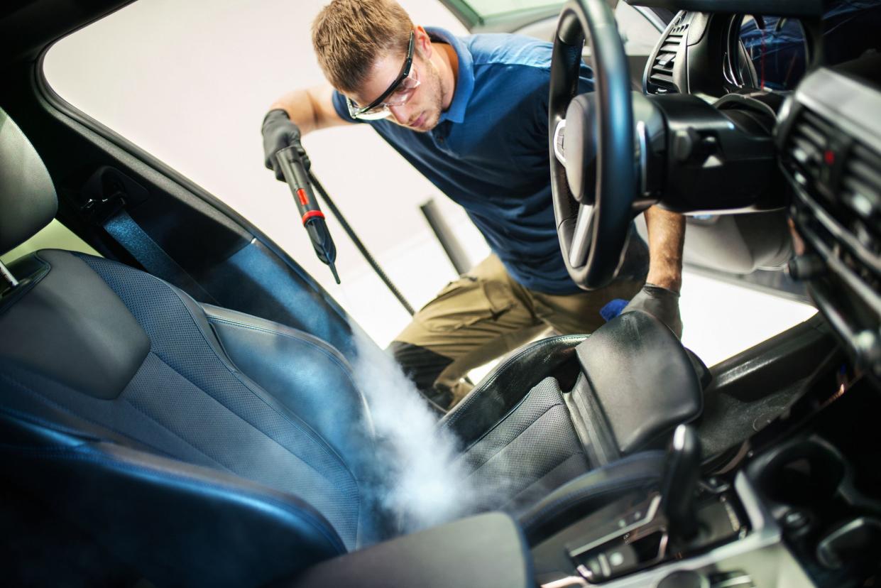 Closeup side view of a young man using fine brush and cleaning AC vents during car interior detailed cleaning.