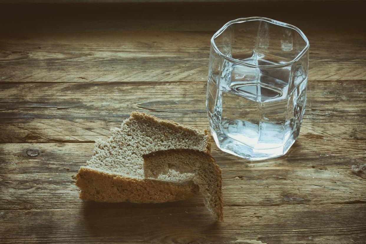 glass of water and hunk black bread crust on old wooden table, concept hunger need
