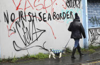 A woman walks her dog past past graffiti with the words 'No Irish Sea Border' in Belfast city centre, Northern Ireland, Wednesday, Feb. 3, 2021. Politicians from Britain, Northern Ireland and the European Union are meeting to defuse post-Brexit trade tensions that have shaken Northern Ireland’s delicate political balance. British Cabinet minister Michael Gove, European Commission Vice President Maros Sefcovic and the leaders of Northern Ireland’s Catholic-Protestant power-sharing government will hold a video conference to discuss problems that have erupted barely a month after the U.K. made an economic split from the 27-nation EU. (AP Photo/Peter Morrison)