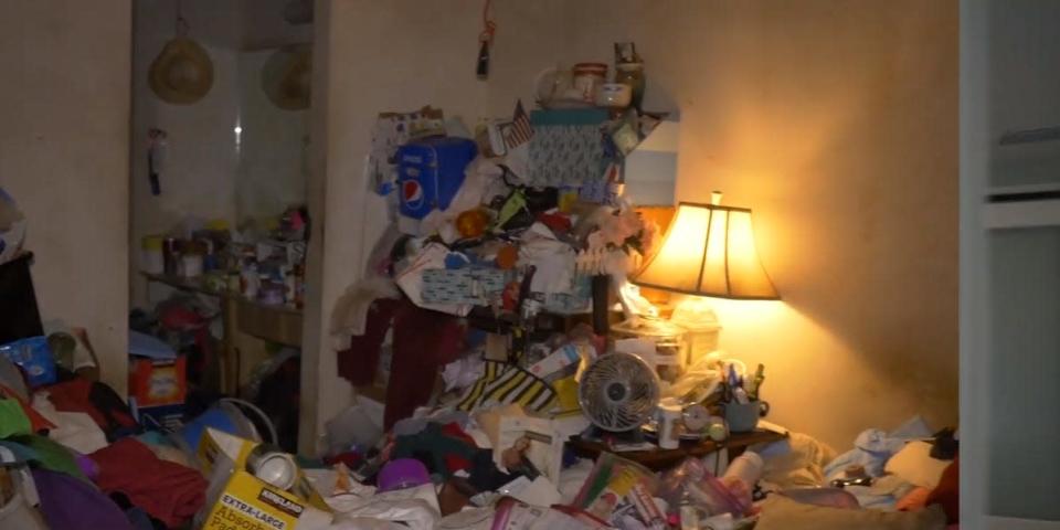 A room lit by a single lamp and filled with a pile of assorted, messy items.