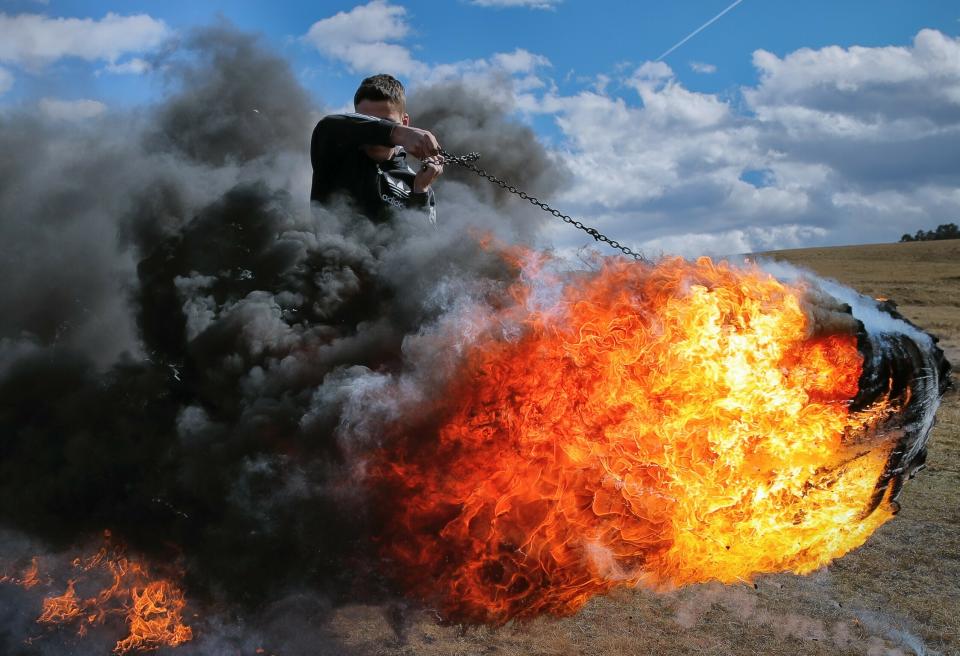 In this photo taken on Sunday, March 10, 2019, a young man spins a burning tire on a metal chain during a ritual marking the upcoming Clean Monday, the beginning of the Great Lent, 40 days ahead of Orthodox Easter, on the hills surrounding the village of Poplaca, in central Romania's Transylvania region. Romanian villagers burn piles of used tires then spin them in the Transylvanian hills in a ritual they believe will ward off evil spirits as they begin a period of 40 days of abstention, when Orthodox Christians cut out meat, fish, eggs, and dairy. (AP Photo/Vadim Ghirda)