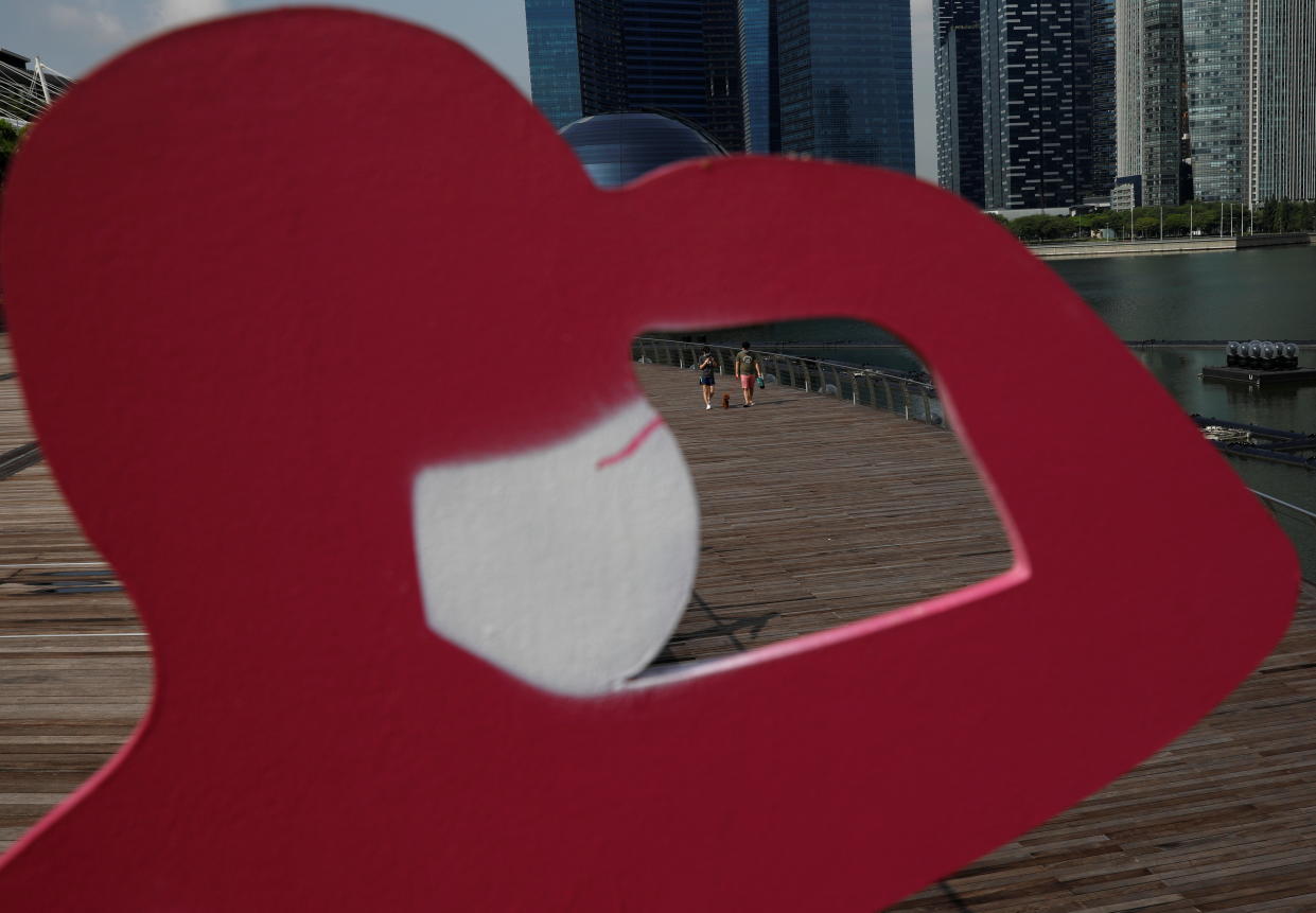 People walk their dog past a sign put up to encourage social distancing along Marina Bay during the coronavirus disease (COVID-19) outbreak, in Singapore, September 29, 2021. REUTERS/Edgar Su