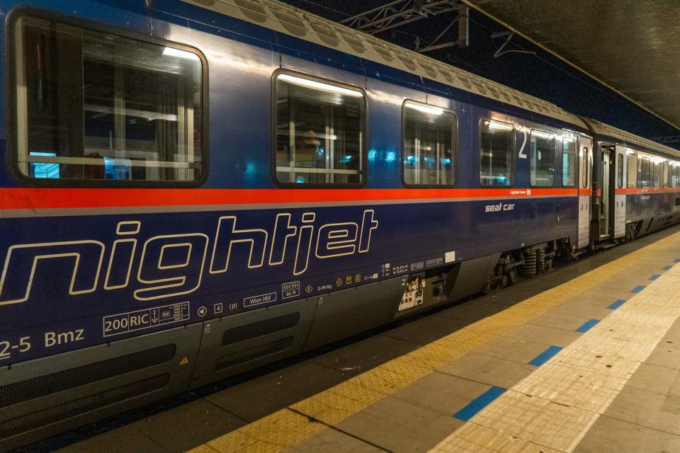 A blue train with a red stripe stopped at a platform at night